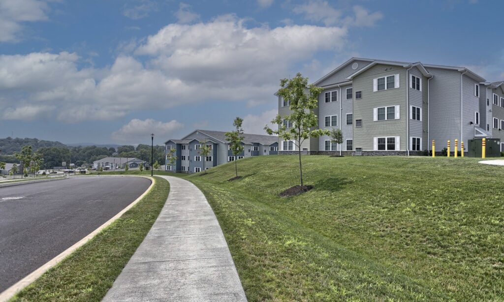 Image of an apartment building with green grass in from of it and a blue sky with clouds above